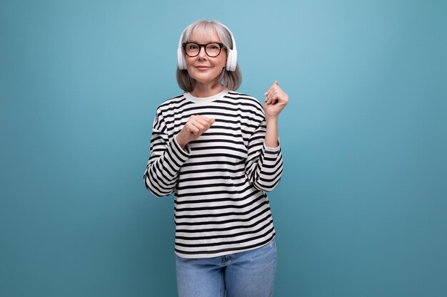 La vieille dame moderne et élégante écoute de la musique dans les écouteurs et danse sur un fond clair avec copie