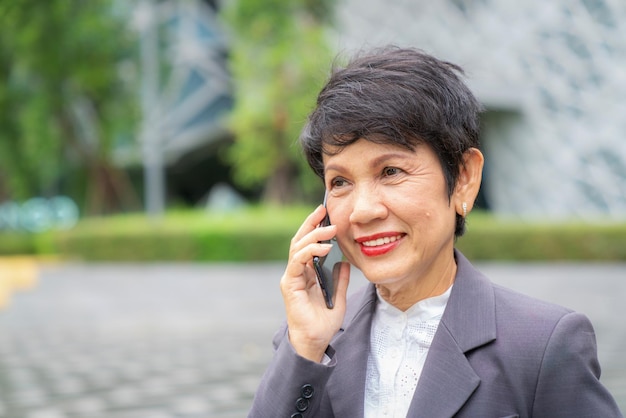 Photo une vieille femme d'affaires asiatique appelle le téléphone portable avec son client devant le bureau de son entreprise.