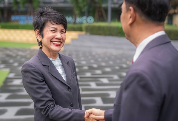 Photo une vieille femme d'affaires asiatique serre la main de son client devant le bureau de son entreprise avec un sourire et une expression