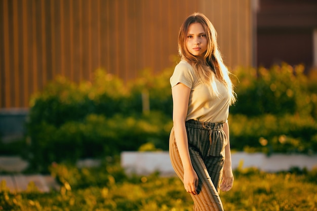 Photo vieille femme de l'année se tient devant le mur d'une maison en bois au coucher du soleil portrait à mi-shot portrait en plein air