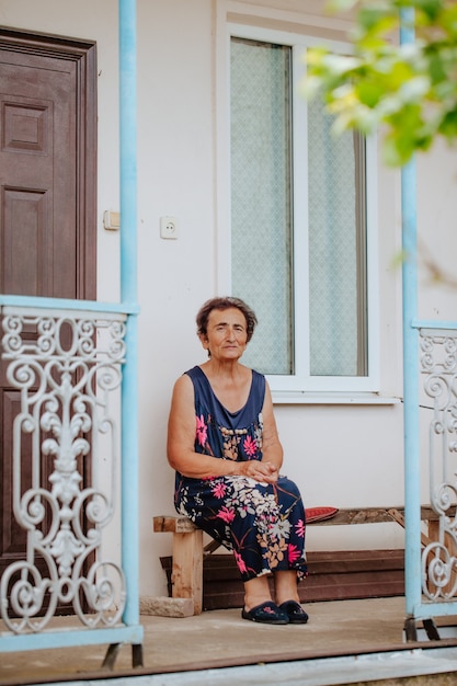 Une vieille femme assise sur un porche avec une balustrade en fer forgé