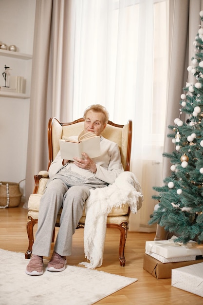 Vieille femme assise près de l'arbre de Noël et lisant un livre