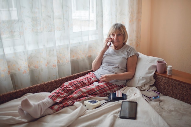 Vieille femme au lit en regardant l'écran de l'ordinateur portable et en consultant un médecin en ligne à la maison, la télésanté