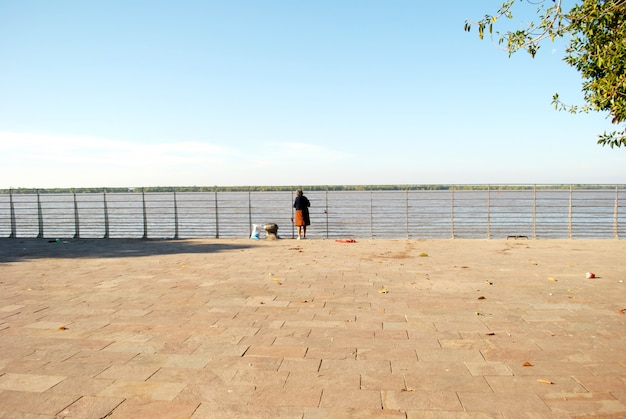 Vieille femme debout devant une rivière. Journée ensoleillée.