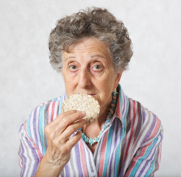 Une vieille femme entre 70 et 80 ans mange du pain séché à grains entiers