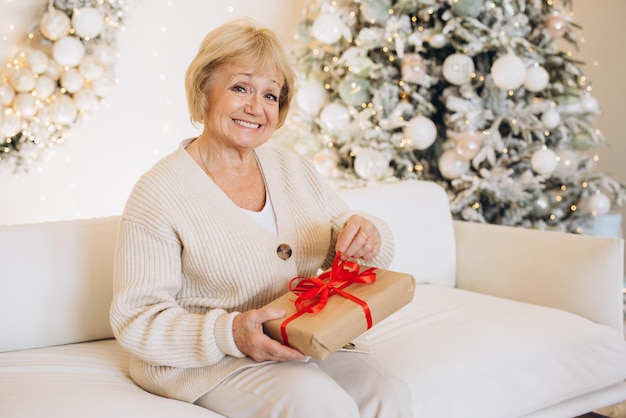 Une vieille femme heureuse tenant un cadeau près de l'arbre de Noël