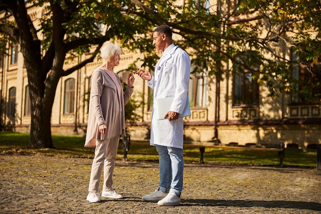 vieille femme irritée en désaccord avec son médecin calme au milieu d'un trottoir