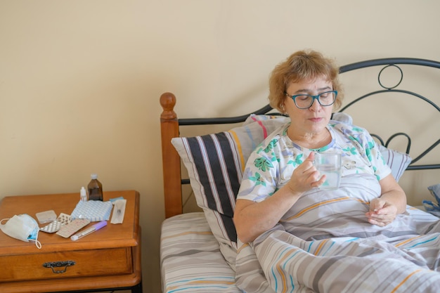 Une vieille femme malade est allongée à la maison dans son lit Un retraité prend un remède contre la maladie et boit un verre d'eau