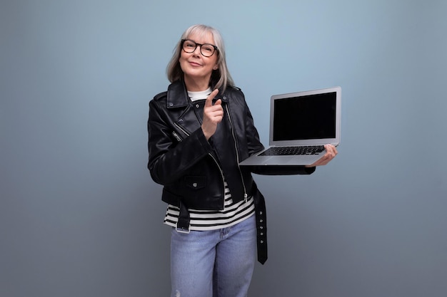 Une vieille femme mature aux cheveux gris fait un excellent travail avec la technique de l'ordinateur portable avec une maquette sur un fond lumineux