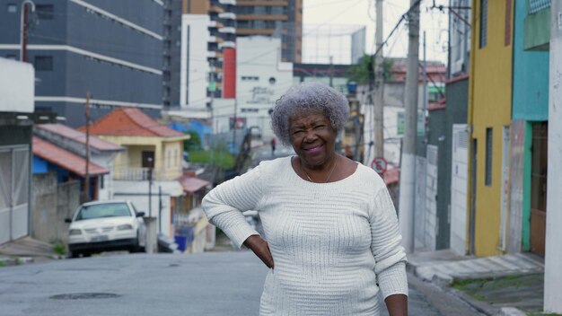 Une vieille femme noire debout à l'extérieur dans la rue urbaine regardant la caméra