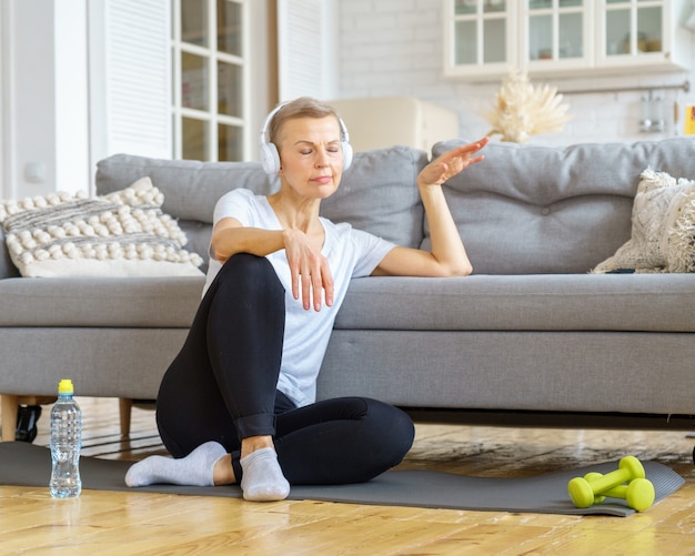 Vieille femme se relaxant après une activité de remise en forme à la maison en écoutant des activités de soulagement du stress de la musique