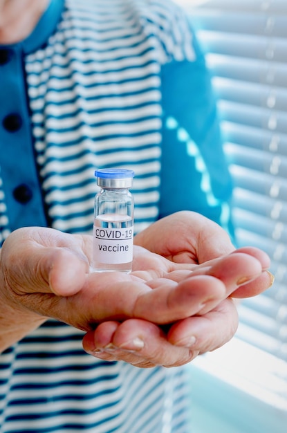 Vieille femme en t-shirt bleu tenant une bouteille en verre de flacon de vaccin pour la vaccination contre COVID-19.