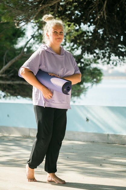 Vieille femme tenant un tapis de yoga et se préparant à pratiquer le yoga ou la méditation à l'extérieur sur la plage de la mer