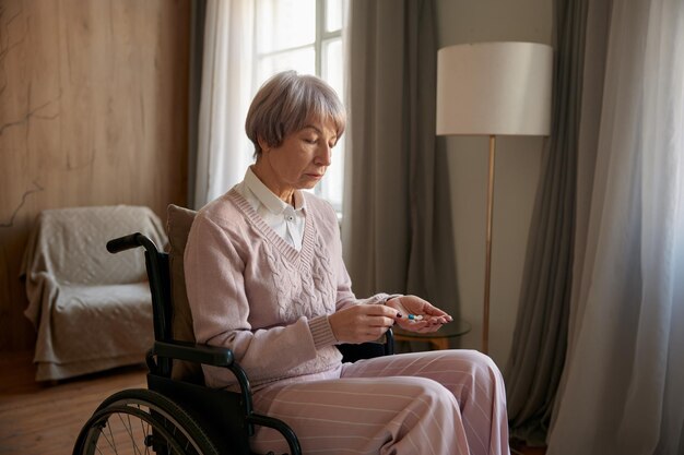 Une vieille femme triste et solitaire en fauteuil roulant prenant des pilules prescrites à l'hospice.