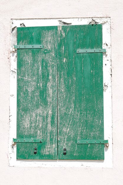 Vieille fenêtre en bois avec volets verts sur un mur peint en blanc, à l'île de Burano, Venise, Italie