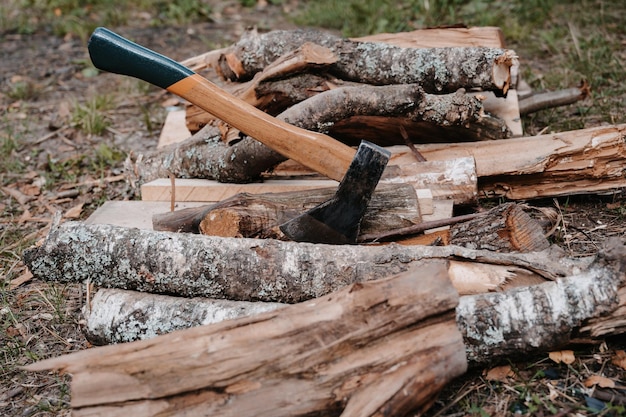 Une vieille hache battue est coincée dans une bûche sur un tas de bois de chauffage Loisirs de plein air Préparation pour le feu de joie