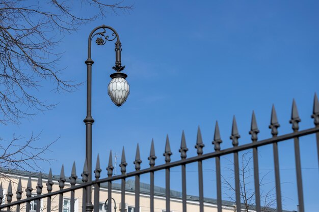 Une vieille lanterne d'éclairage sur un poteau dans le contexte d'une clôture avec des lances pointues