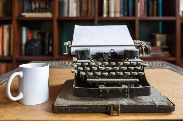 Vieille machine à écrire poussiéreuse vintage avec feuille de papier blanc et tasse de café