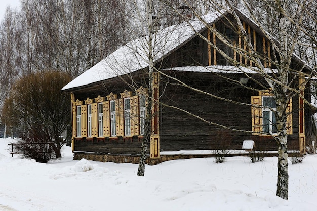 Vieille maison en bois faite de rondins gris Avec de belles fenêtres et volets jaunes Paysage russe d'hiver Arbres couverts de neige Ancien village russe abandonné couvert de neige