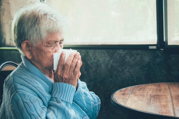 Vieille personne toussant couvrant la bouche avec un mouchoir à l'intérieur d'une maison. Elle a la grippe, des symptômes d'allergie, une bronchite aiguë, des infections pulmonaires ou une pneumonie.