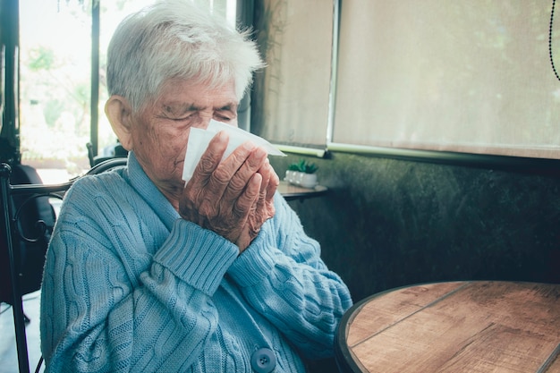 Photo vieille personne toussant couvrant la bouche avec un mouchoir à l'intérieur d'une maison. elle a la grippe, des symptômes d'allergie, une bronchite aiguë, des infections pulmonaires ou une pneumonie.