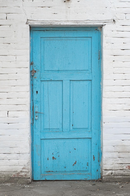 Vieille porte en bois bleu délabré sur un mur de brique blanche