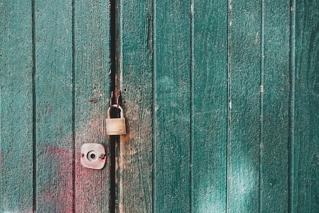 La vieille porte en bois verte est verrouillée avec un cadenas. vertical.