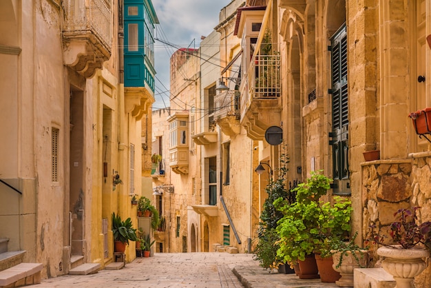 Vieille rue médiévale avec des bâtiments jaunes, de beaux balcons et des pots de fleurs à Birgu, La Valette, Malte
