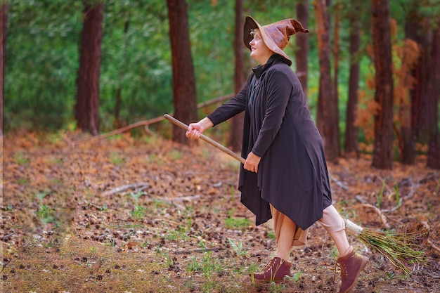 Une vieille sorcière coiffée d'un chapeau dans les bois, assise sur un balai, veut voler.