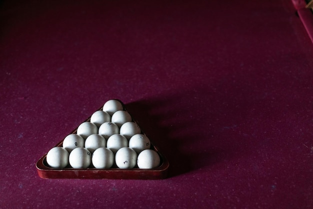 Une vieille table de billard avec un tissu rouge et un ensemble de boules de billard blanches dans un cadre triangulaire en bois