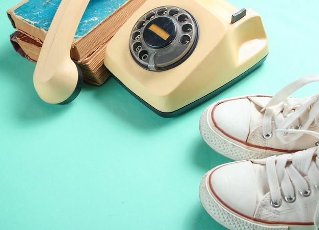 Vieilles baskets, téléphone rotatif rétro et une pile de vieux annuaires téléphoniques sur fond de couleur menthe