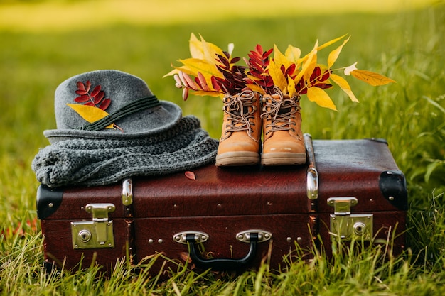 Vieilles bottes, chapeau de feutre et écharpe tricotée sur la valise vintage marron dans la forêt d'automne