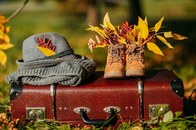 Vieilles bottes, chapeau de feutre et écharpe tricotée sur la valise vintage marron dans la forêt d'automne