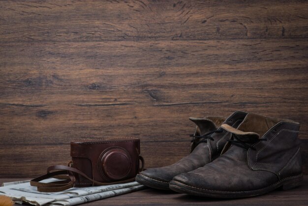 Vieilles chaussures en cuir marron usées avec appareil photo et journal sur fond sombre