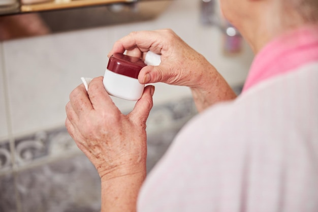 Vieilles mains féminines tenant un pot de crème cosmétique