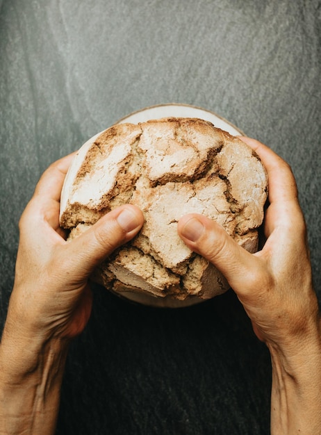 Vieilles mains préparant du pain artisanal et biologique fraîchement cuit sur une table rustique Cuisine maison Pain au levain avec croûte croustillante sur une étagère en bois Concept de produits de boulangerie Restaurant et produits