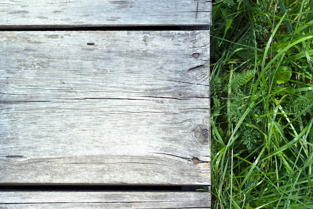 vieilles planches de bois altérées avec de l'herbe verte comme fond d'été