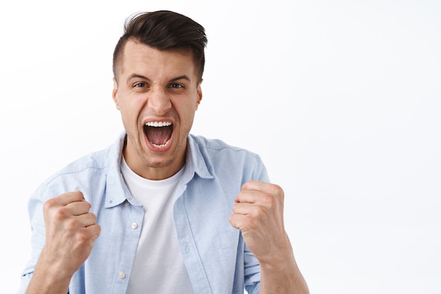 Viens te battre. Portrait d'un bel homme excité, criant en tant qu'enracinement pour l'équipe, regardant un match de sport, serrant les poings et criant, célébrant la victoire, triomphant du score, remportant un prix