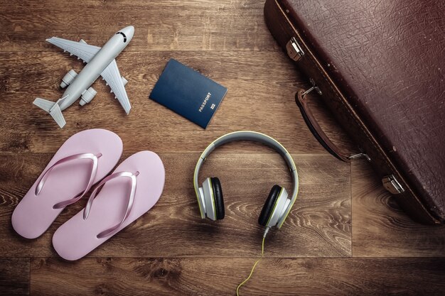 Vieux bagages, écouteurs, tongs, figurine d'avion, passeport sur plancher en bois