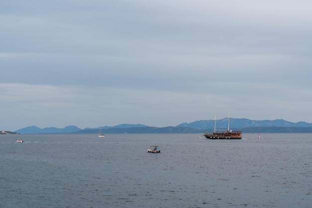 Un vieux bateau en bois avec de nombreux touristes à bord dans la mer Adriatique C'est le soir De hautes montagnes à l'horizon De petits yachts et bateaux naviguent à proximité de la Croatie