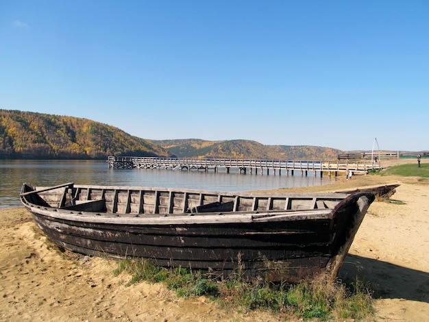 Vieux bateau en bois sur le pont de rivage sablonneux au-dessus des montagnes de la rivière couvertes de forêts journée d'automne