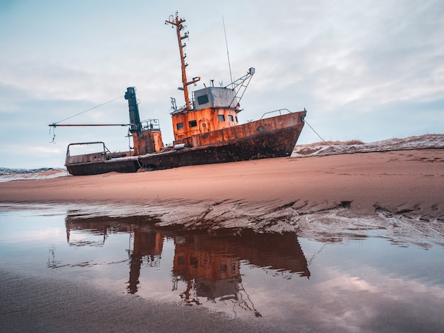 Vieux bateau de pêche rouillé échoué sur une plage de sable dans la mer de Barents