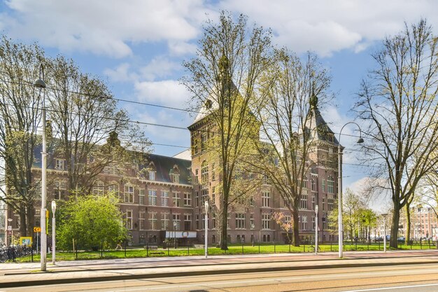 Un vieux bâtiment en brique au milieu d'Amsterdam avec des arbres bordant la rue et des voitures garées sur le côté