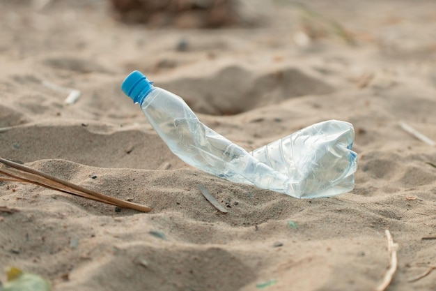 Vieux bleu écrasé froissé écrasé bouteille en plastique vide jeté sur une plage de sable problème écologique recyclage jour de la terre