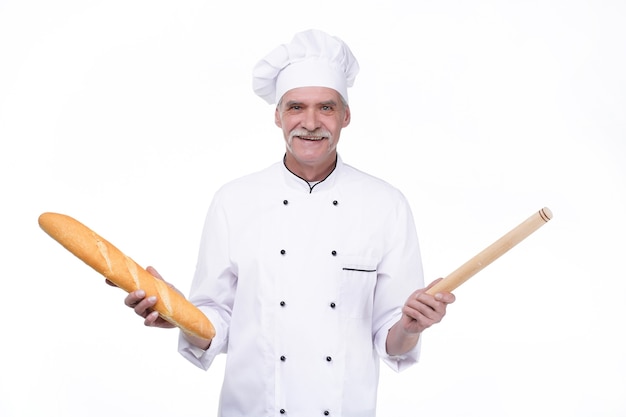 Vieux boulanger professionnel en uniforme tenant des baguettes tout en restant sur un mur blanc