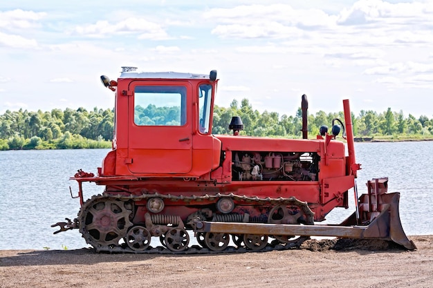 Vieux bulldozer rouge de tracteur sur un fond de la rivière et du ciel