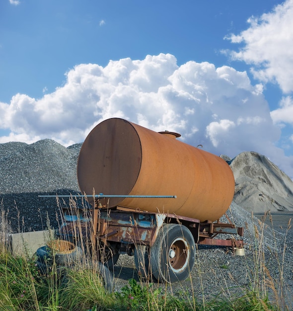 Vieux camion-citerne en décomposition sur le chantier de construction Réservoir d'eau rouillé près d'un tas de béton et de ciment Vieux réservoir de remorque d'eau rouillé abandonné près d'un tas de sable et de gravier dans l'industrie du bâtiment