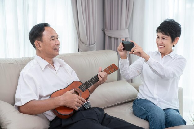 Photo un vieux couple asiatique chante une chanson avec joie et émotion et joue du ukulélé ensemble dans le salon de leur maison.