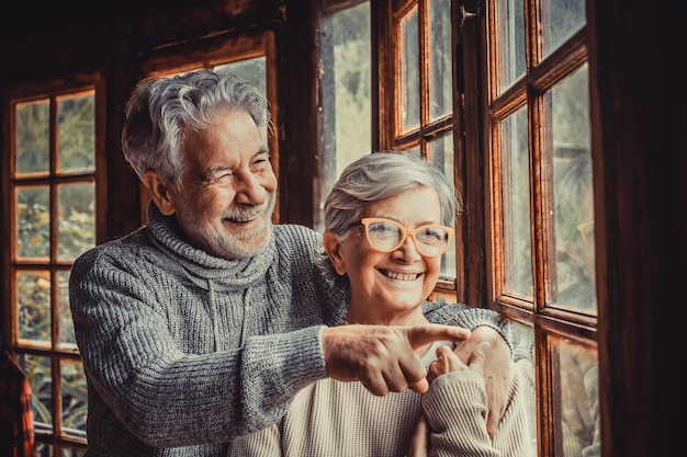 Vieux couple caucasien passant du temps libre en regardant par la fenêtre à la maison Mari aimant pointant et montrant quelque chose d'intéressant à sa femme depuis la vitre transparente de la porte