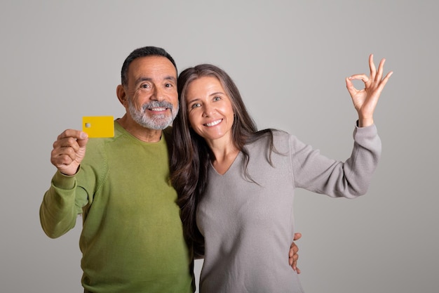 Vieux couple européen positif avec carte de crédit profiter des achats en ligne à distance montrer le signe de la main ok
